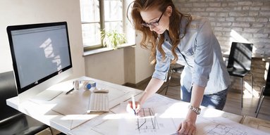 Eine Frau steht an einem Bürotisch und makiert eine Technische Zeichnung